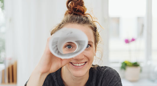 Eine junge Frau schaut durch ein Fernrohr aus Papier und lacht.