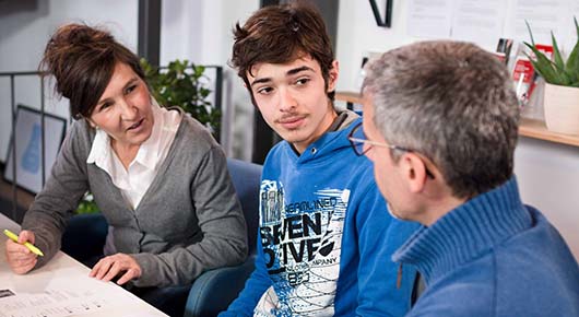 Eine Beratungssituation in der Jugendberufsagentur. Ein junger Mann sitzt mit zwei Fachkrften ber einem Lebenslauf zusammen.