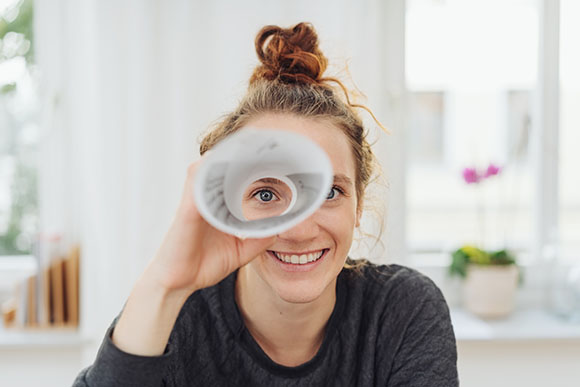 Junge Frau schaut durch ein zum Fernrohr geformtes Stck Papier und lchelt.