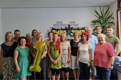 Gruppe mit Menschen vor Wand mit groem Logo hlt einen goldenen Luftballon