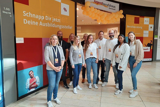 Gruppenfoto von Mitarbeitenden vor dem dekorierten Eingang eines Pop-up-Stores