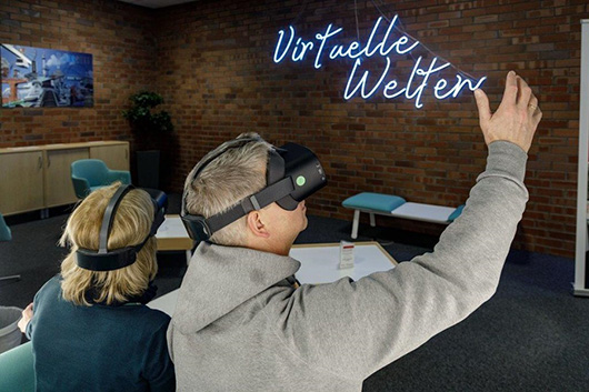 Zwei Menschen mit VR-Brillen vor einem Leuchtschild Virtuelle Welten