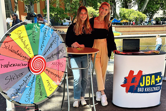 Zwei Frauen an einem Informationsstand im Freien mit einem groen Glcksrad