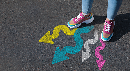 Eine Person in Turnschuhen, von denen vier auf den Asphalt gemalte Pfeile ausgehen Eine Person in Turnschuhen, von denen vier auf den Asphalt gemalte Pfeile ausgehen