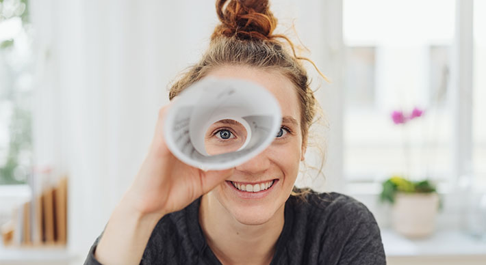 Eine junge Frau schaut durch ein Fernrohr aus Papier und lacht.